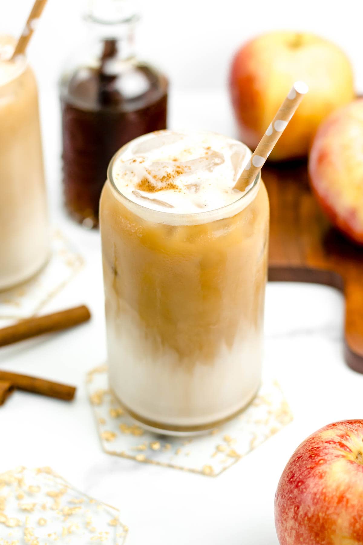 A coffee drink with a tan paper straw near apples on a wooden cutting board.