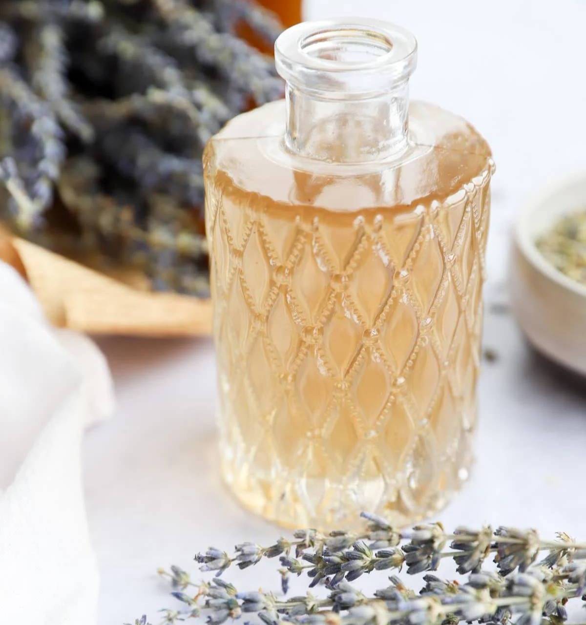 A decorative glass bottle holds a pale syrup near dried lavender.