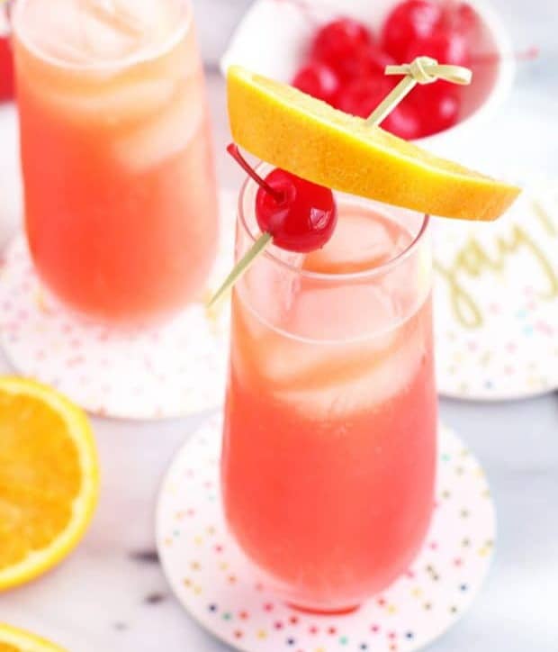 A pink drink in a stemless champagne glass topped with fruit on a bamboo skewer.
