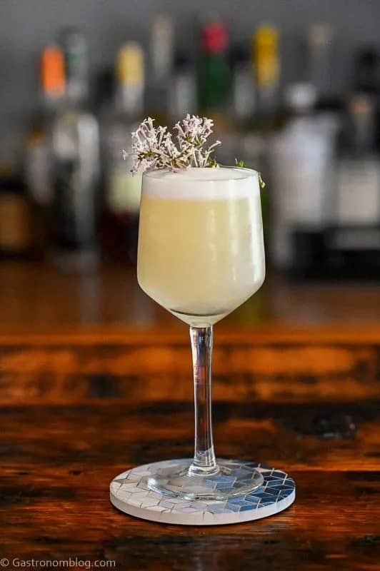 A stemmed glass holds a pale yellow drink topped with flowers. 