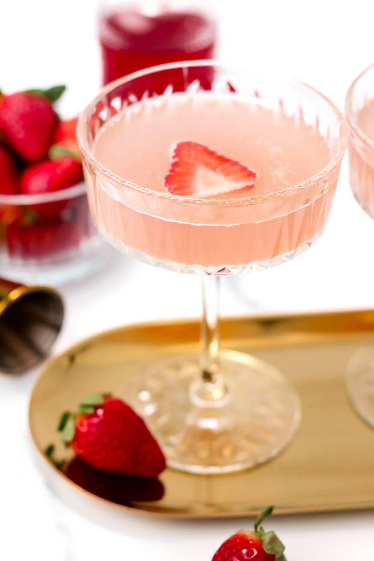 A strawberry mocktail on a gold, round oval tray with a strawberry slice floating on the top.