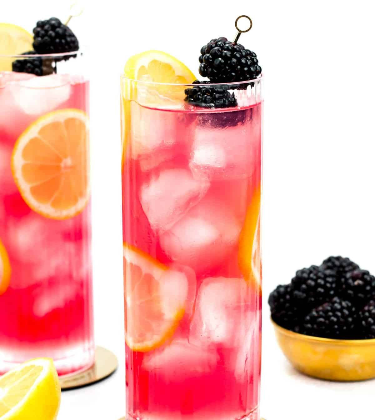 Two pink cocktails sit near a bowl of blackberries.