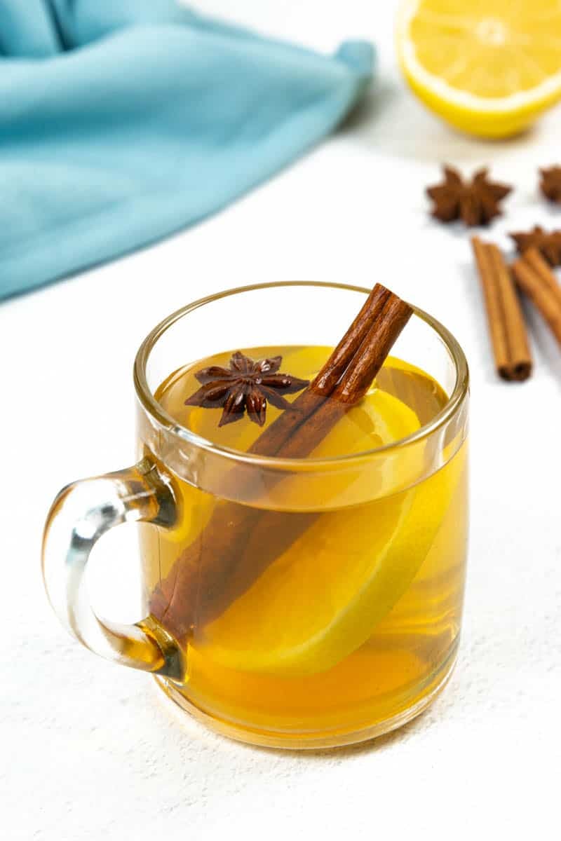 A hot cocktail in a clear glass mug with lemon and whole spices.