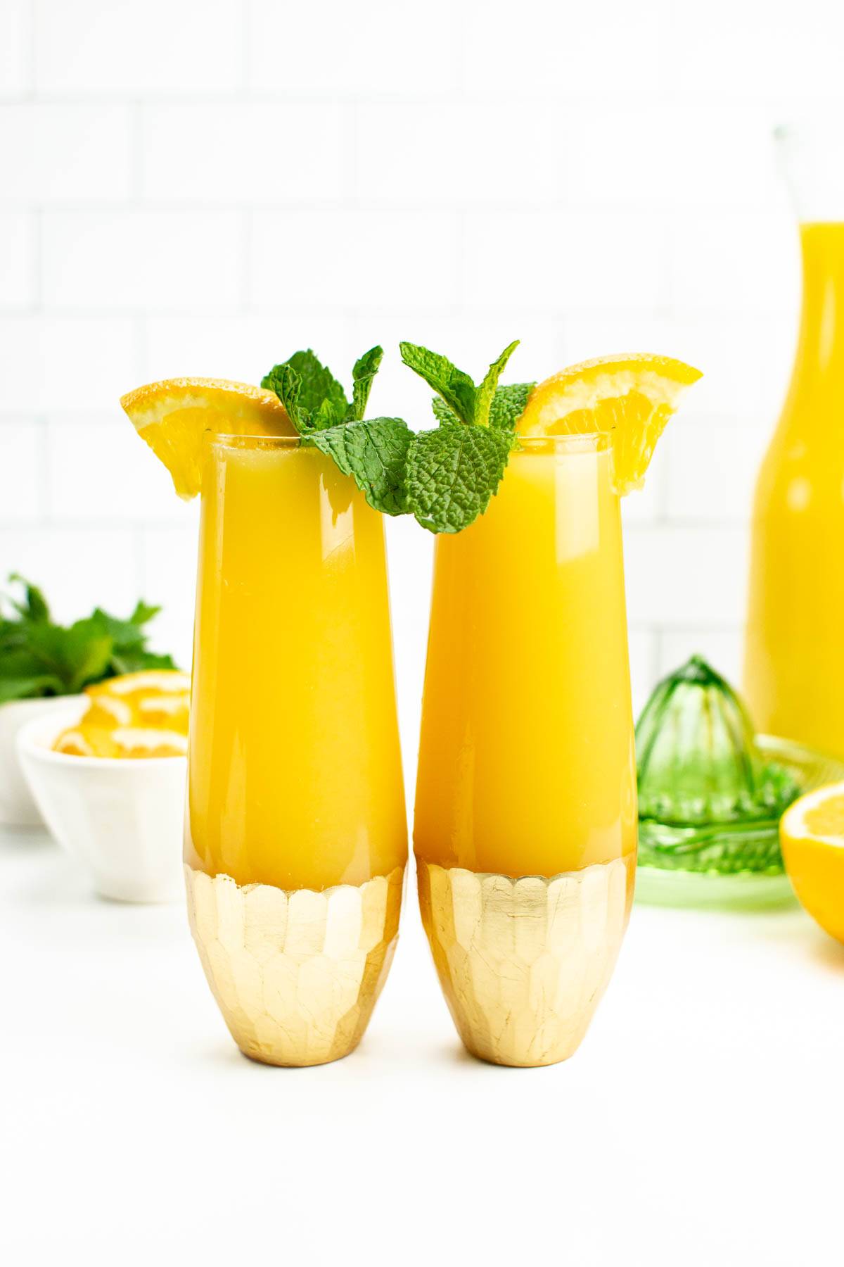 Two orange juice drinks sit side by side in stemless champagne glasses.
