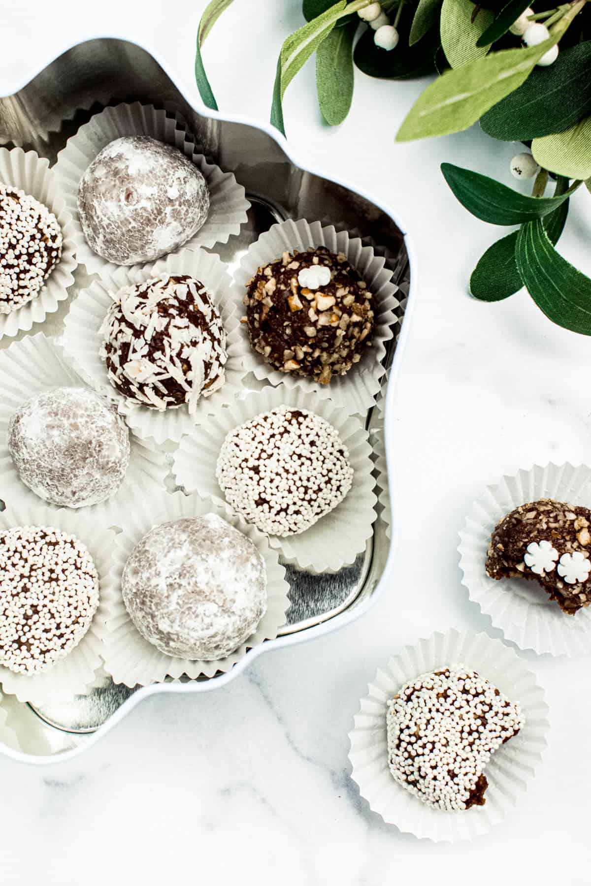 Overhead view of rum balls in a cookie tin on a white marble surface.