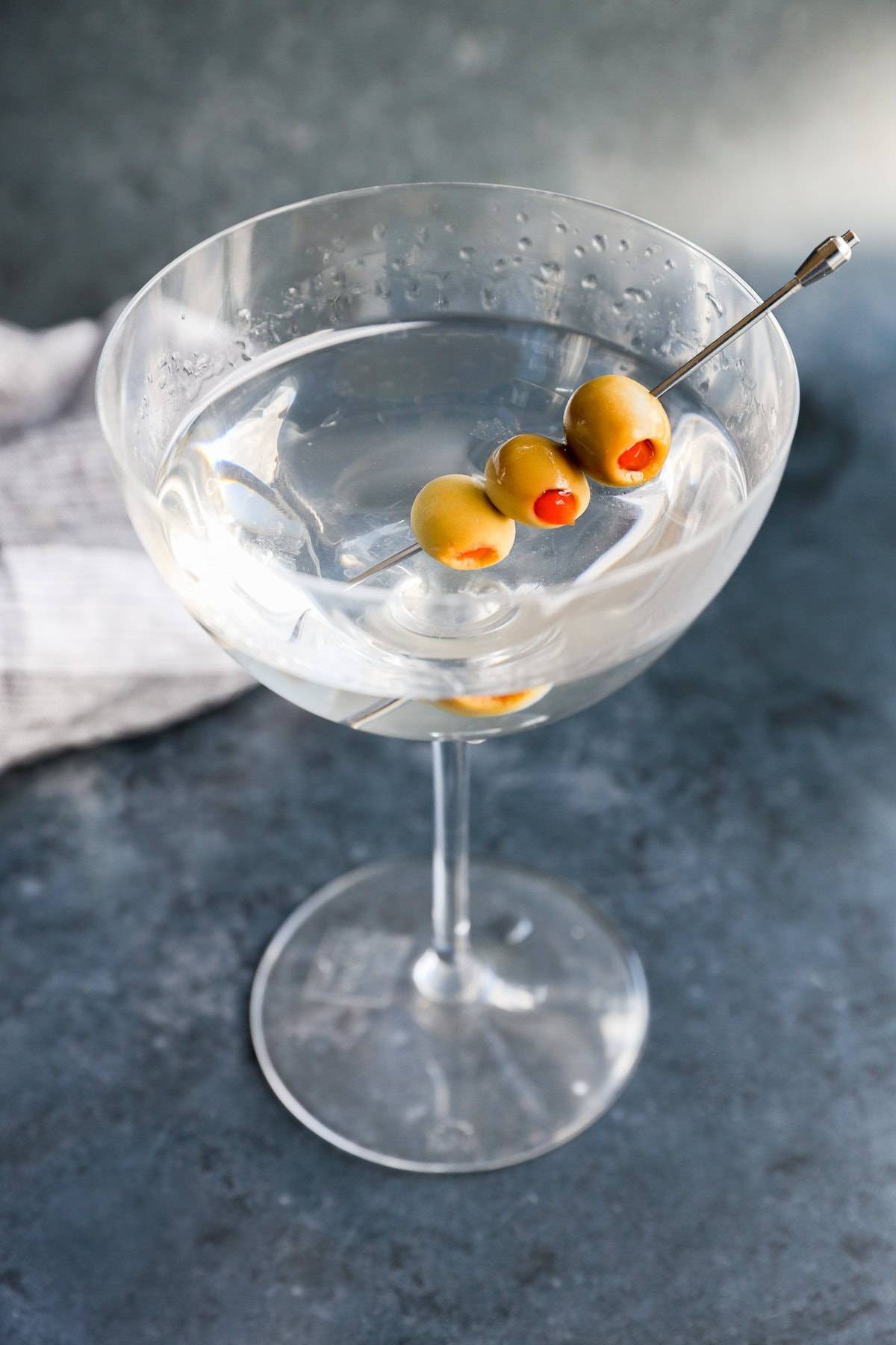 Overhead view of a stemmed glass holding a clear cocktail and three olives on a silver cocktail pick.