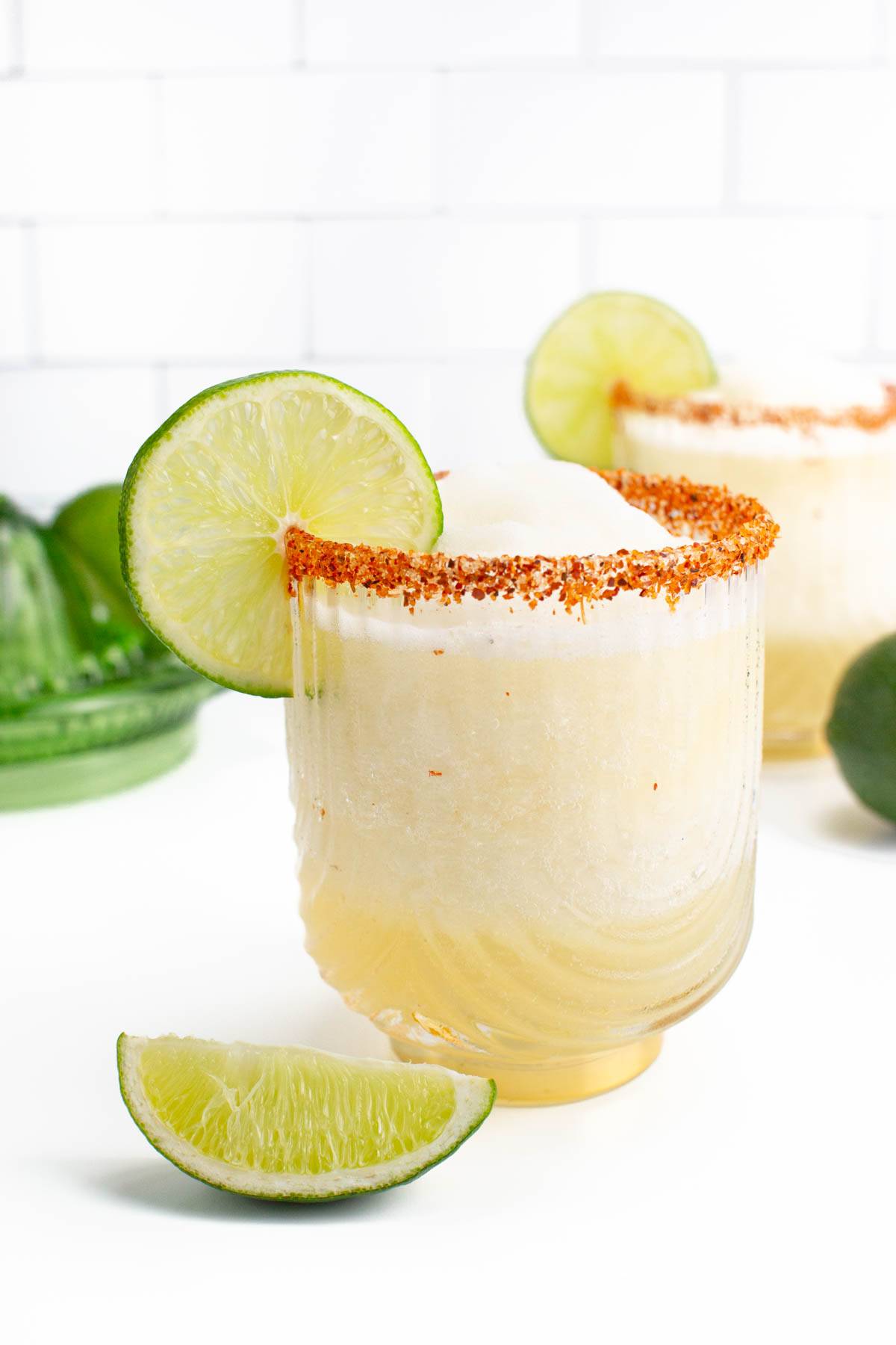 A frozen margarita rimmed with orange salt and a lime wedge as a garnish.