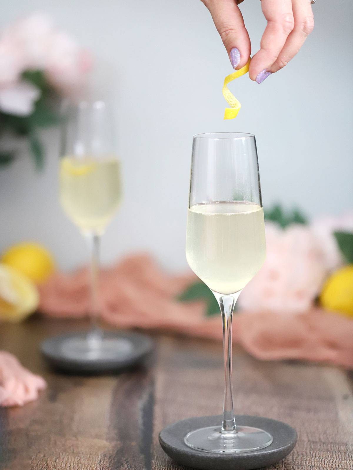 A lemon twist is being lowered into a stemmed champagne glass.