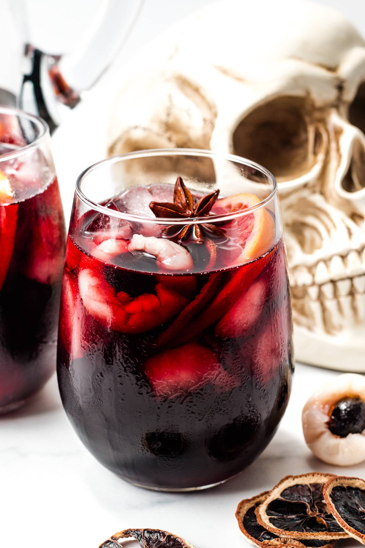 A red drink garnished with eyeballs made of fruit sits in front of a decorative skull.
