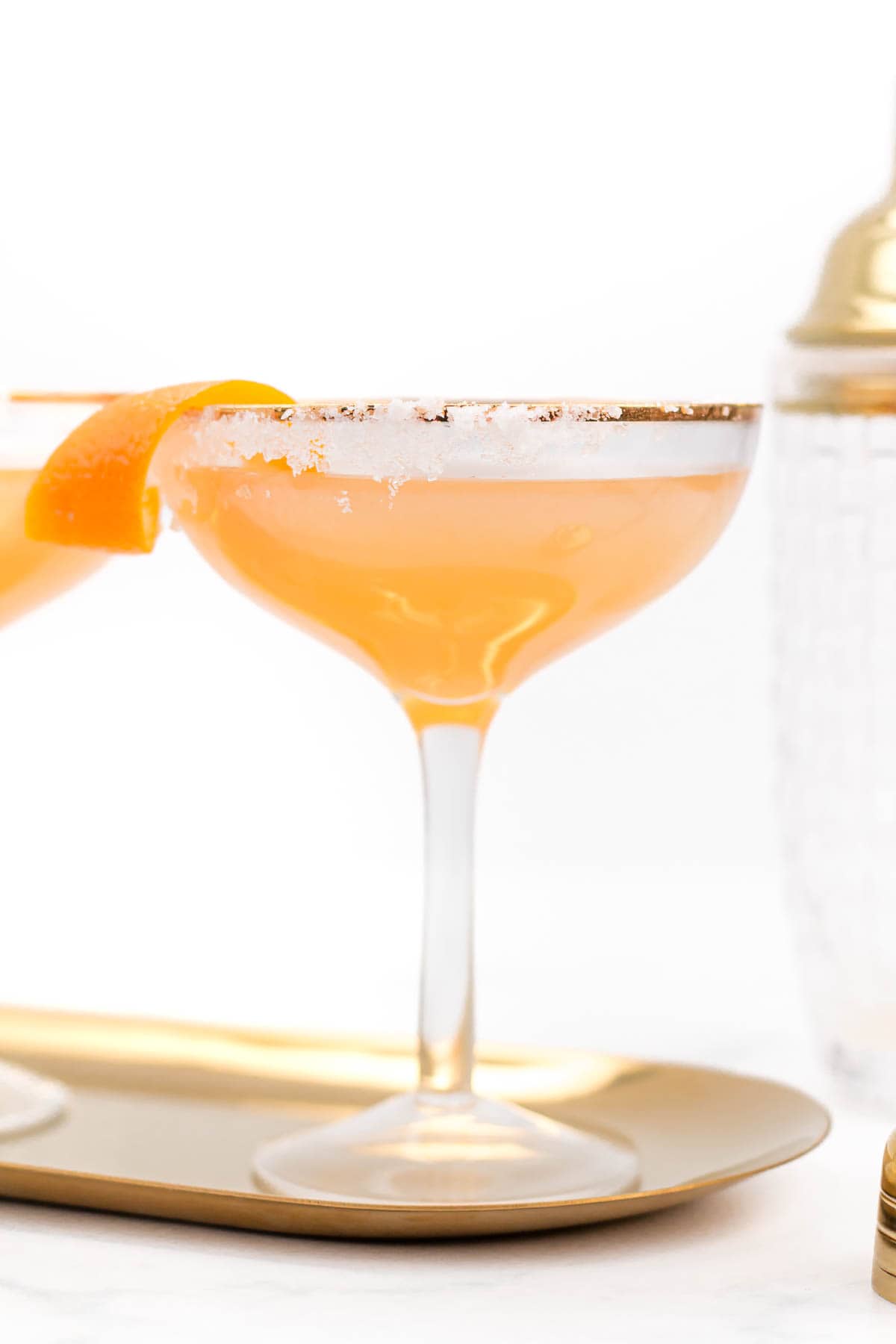 An orange cocktail in a stemmed glass on a gold oval tray.