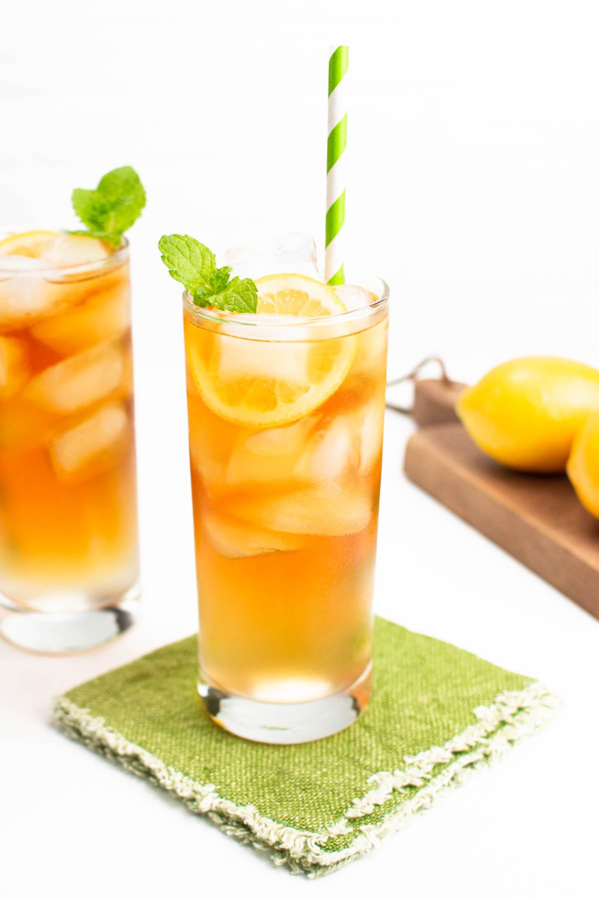 An iced tea drink in a tall glass topped with a lemon round and mint sprig.