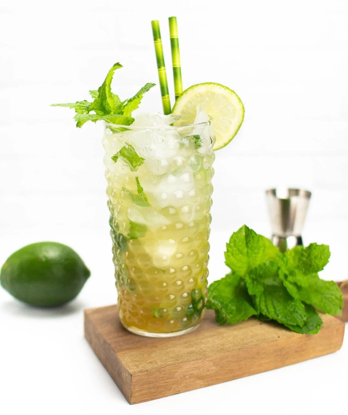 A glass holds a pale green drink with mint and limes.