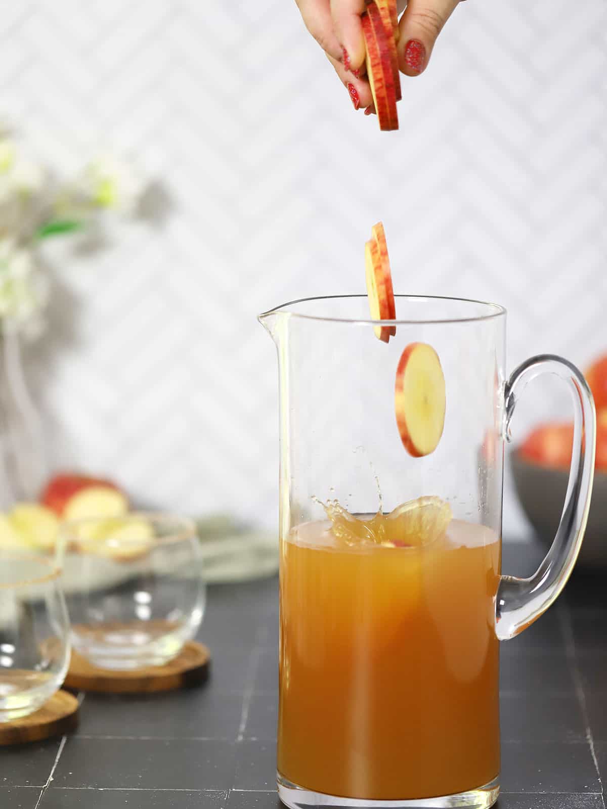 Apple rounds being dropped from above into a clear pitcher with apple cider