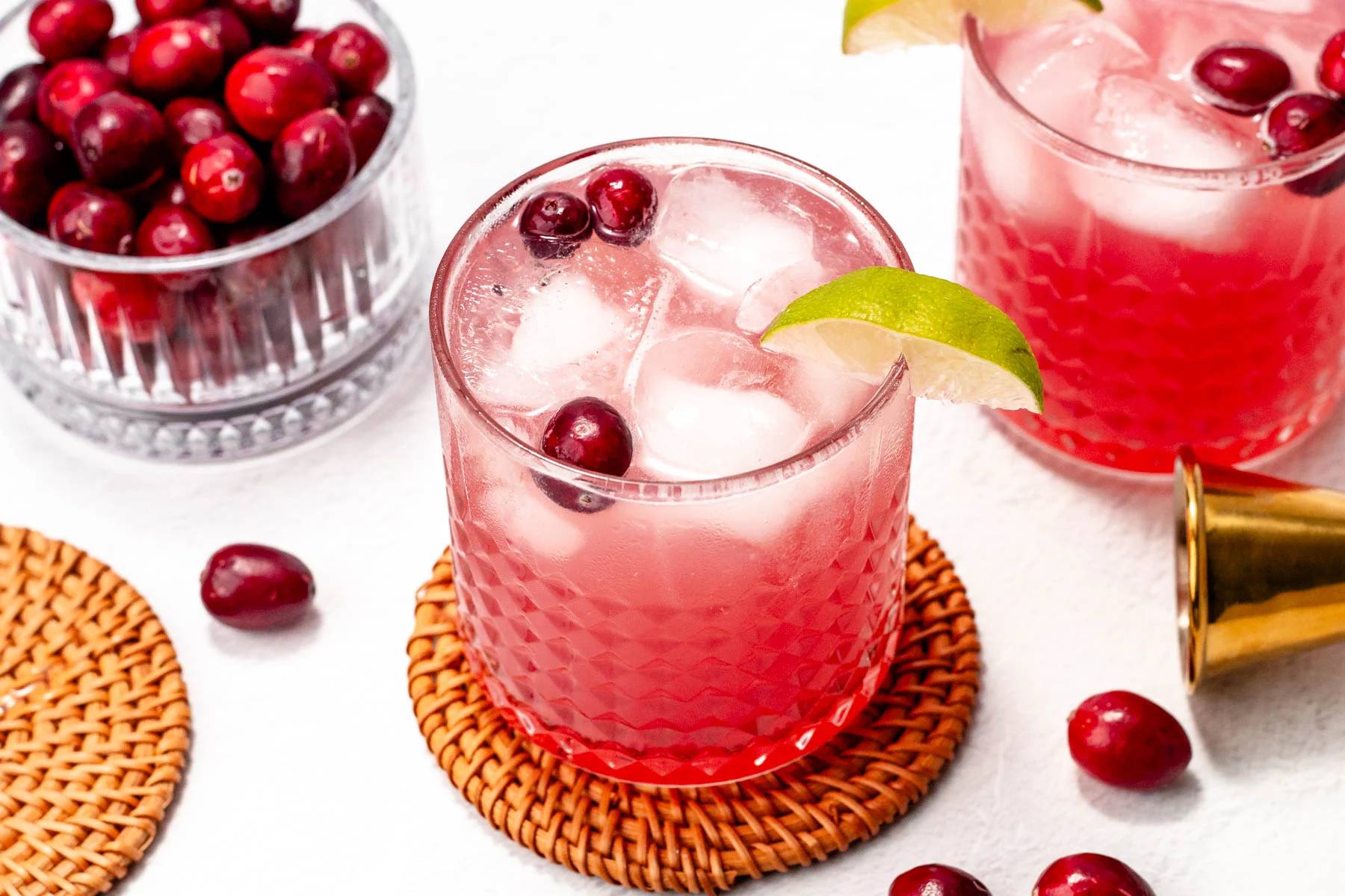 A red cranberry cocktail with whole cranberries and a lime wedge.