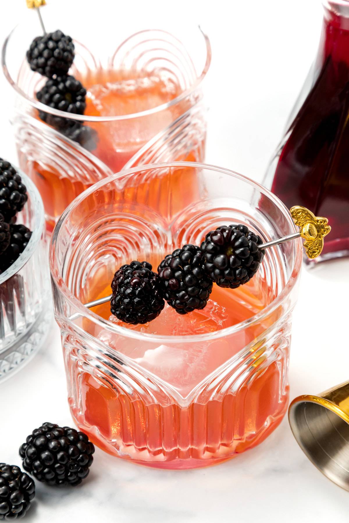 A pink drink garnished with blackberries on a cocktail pick.