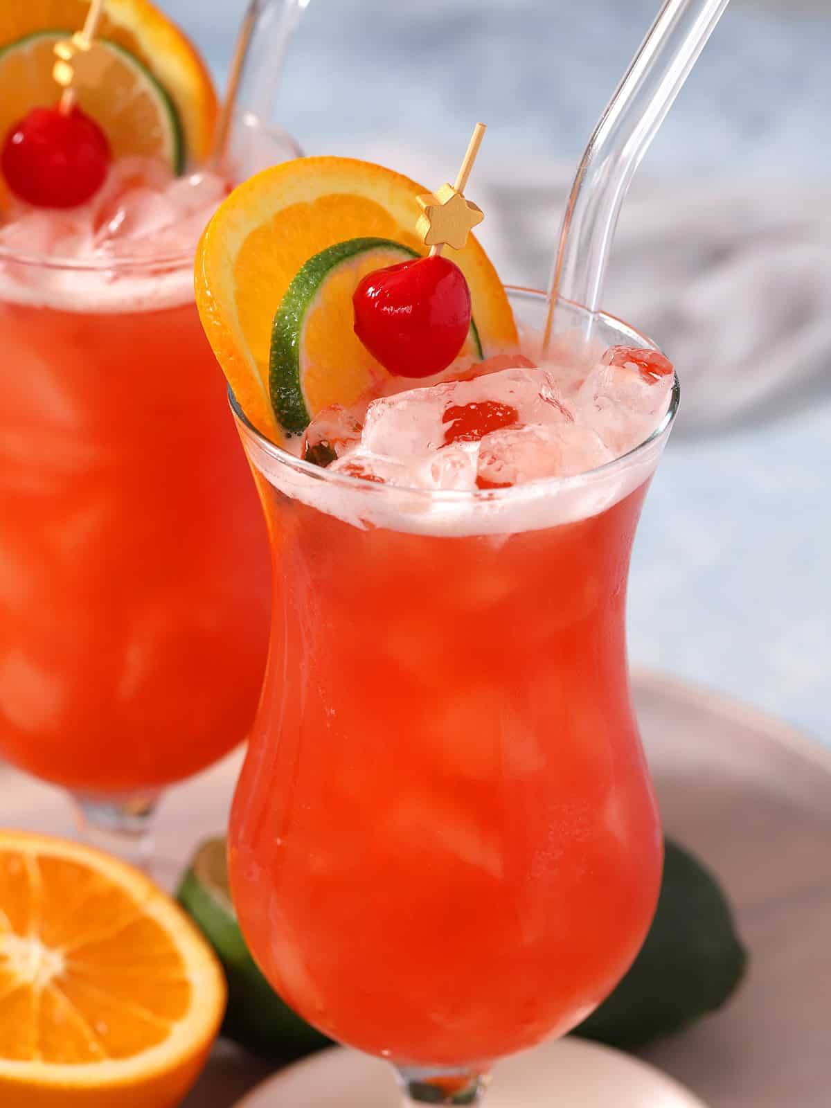 A red drink in a hurricane glass topped with fruit slices.