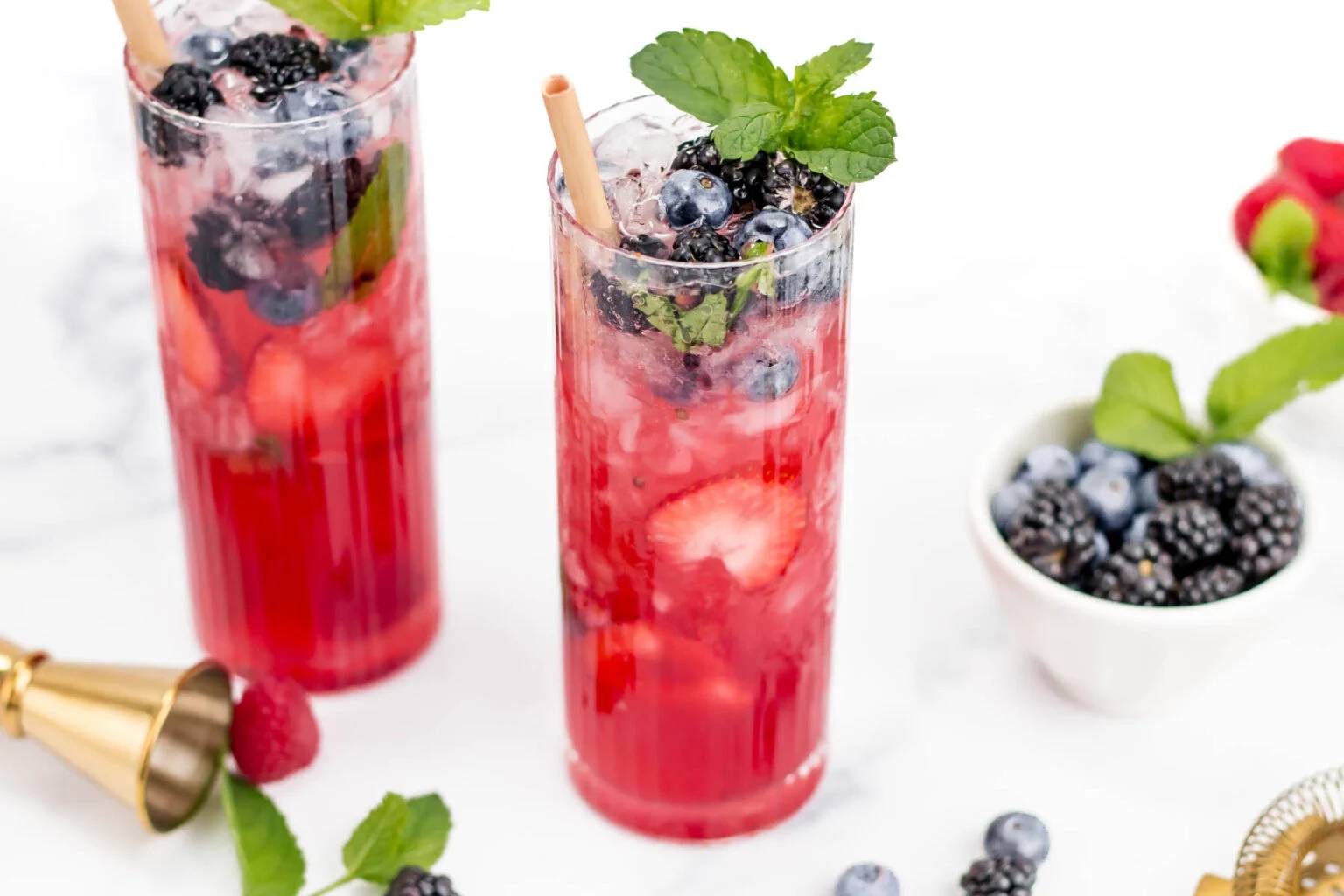 Two red cocktails topped with blueberries and a sprig of mint.