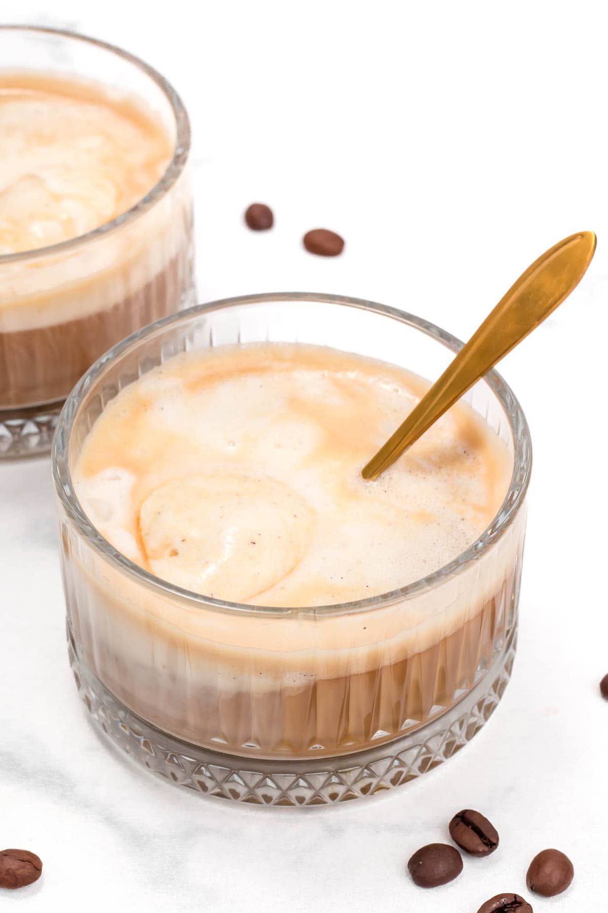 A glass bowl holds a creamy coffee drink with a gold spoon.