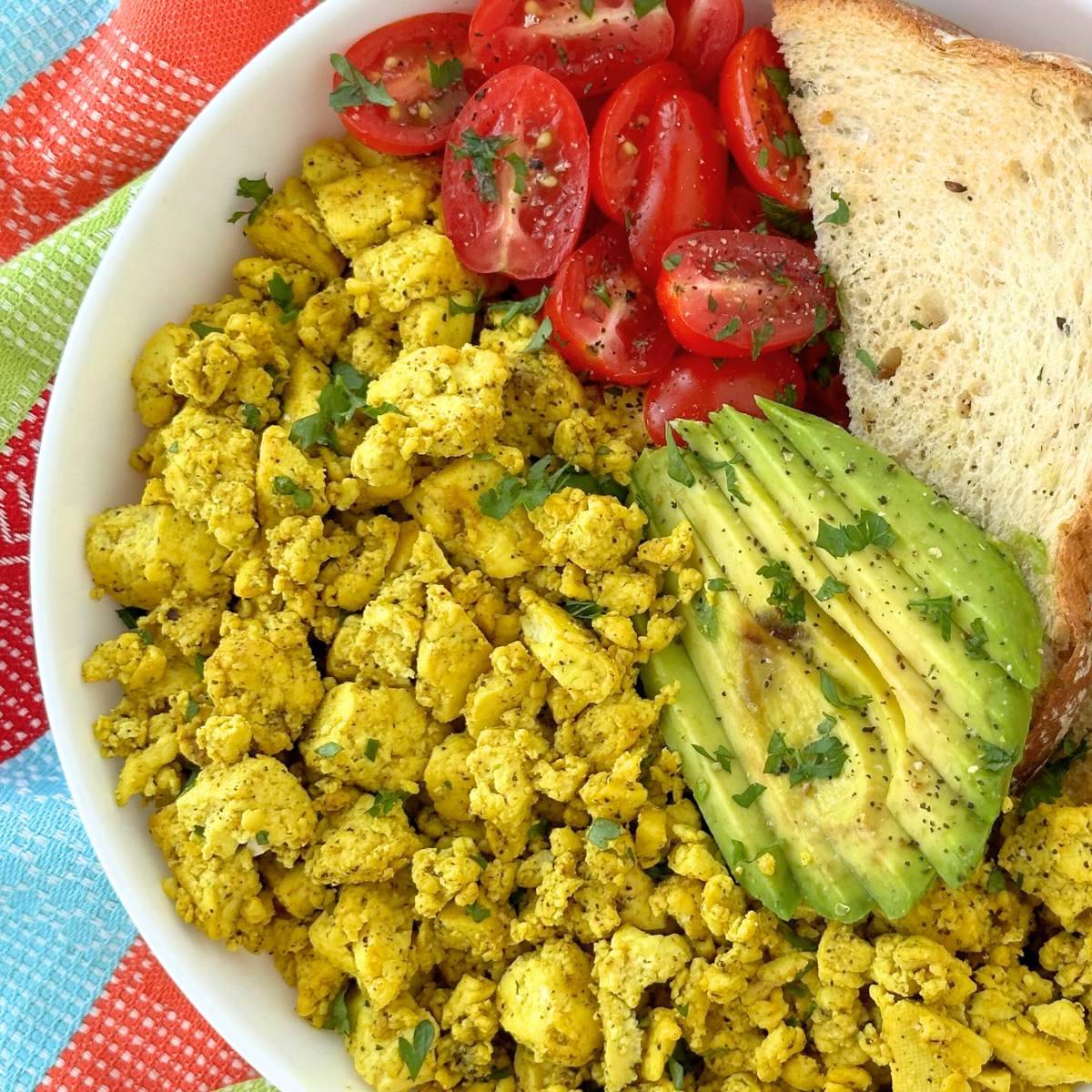 Tofu scramble with sliced avocado, tomato, and bread.