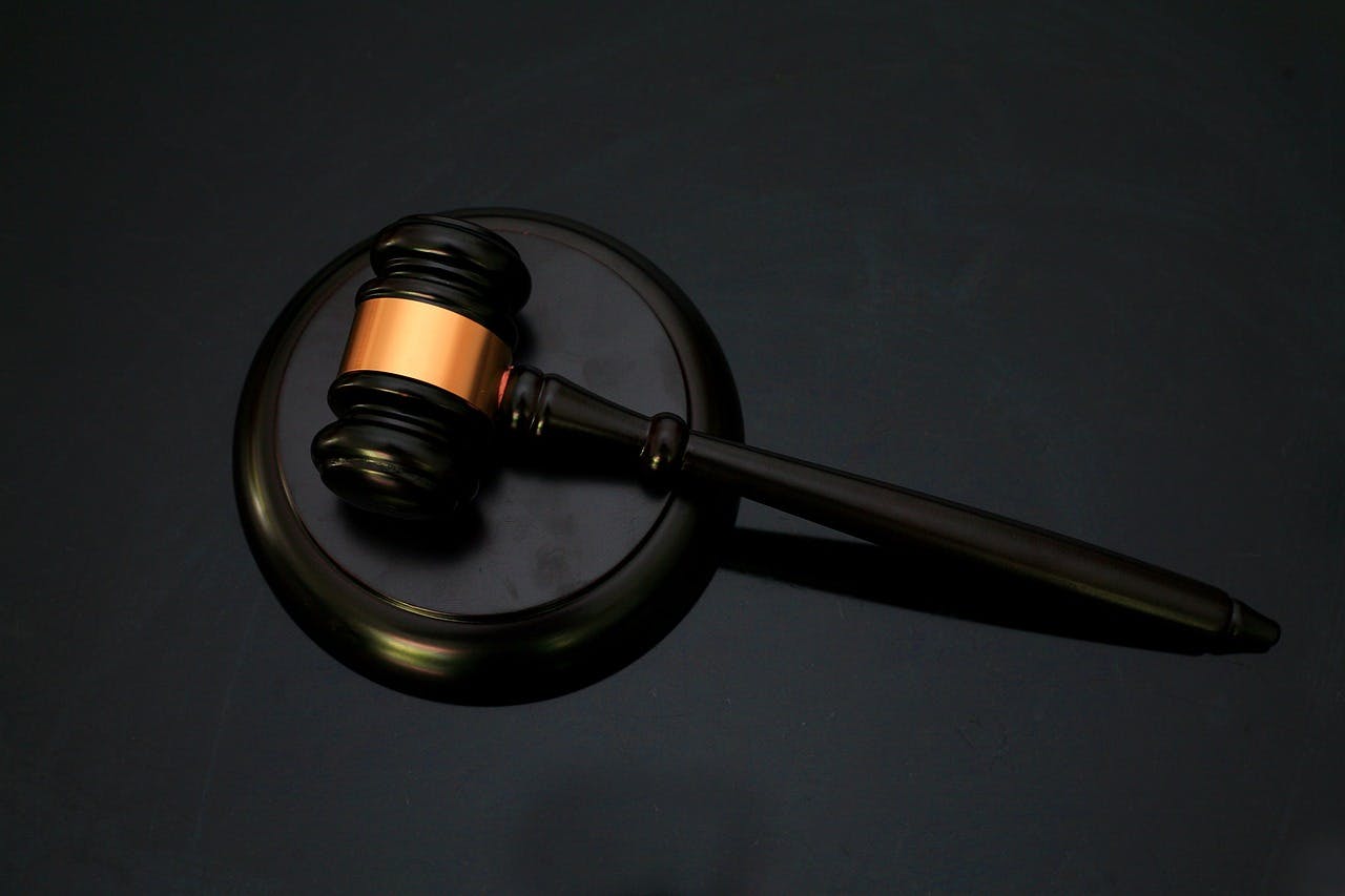 A black and gold gavel sits on a black pedestal. The background is also black. The gold part of the gavel is in the middle joining band.