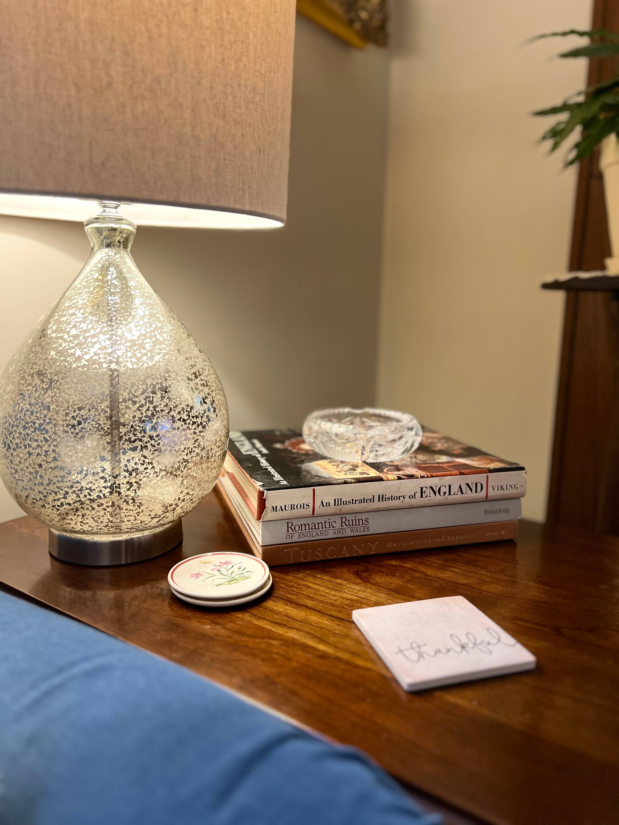Lamp, stack of books and crystal ash tray on a side table