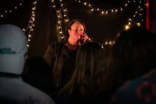 Joanna Evervenn performing to a crowd with their hand up to their face. Image by Fleassy Malay. 