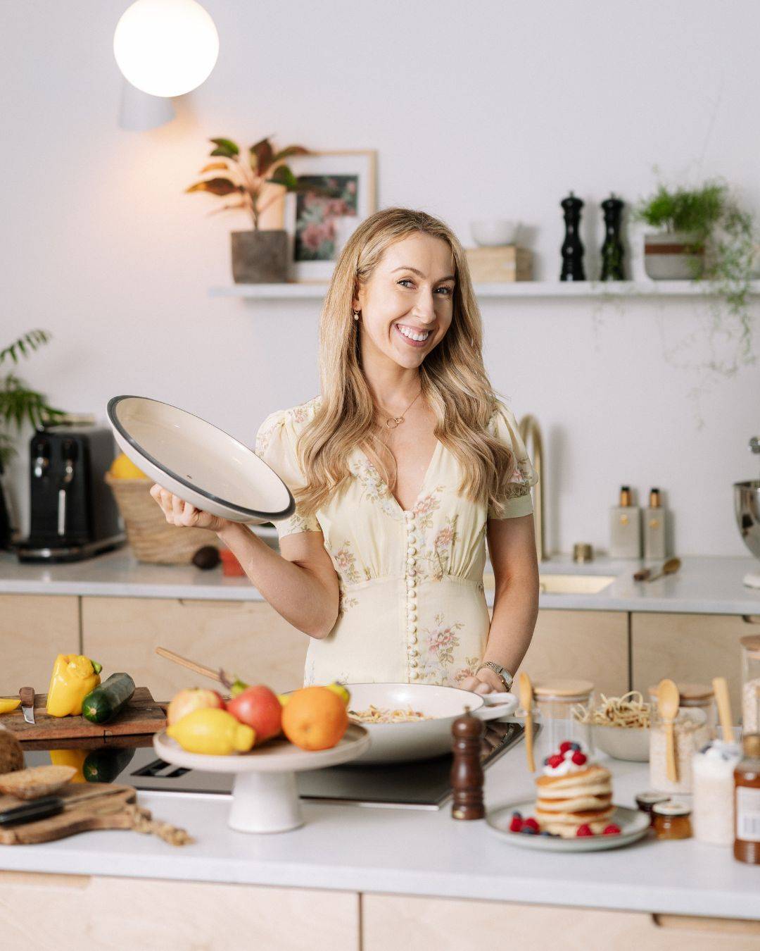 Online Dietitian Maria Lucey in the kitchen lifting a pan surrounded by healthy food.