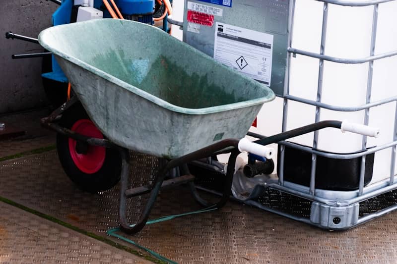 A green wheelbarrow next to a large white tank.