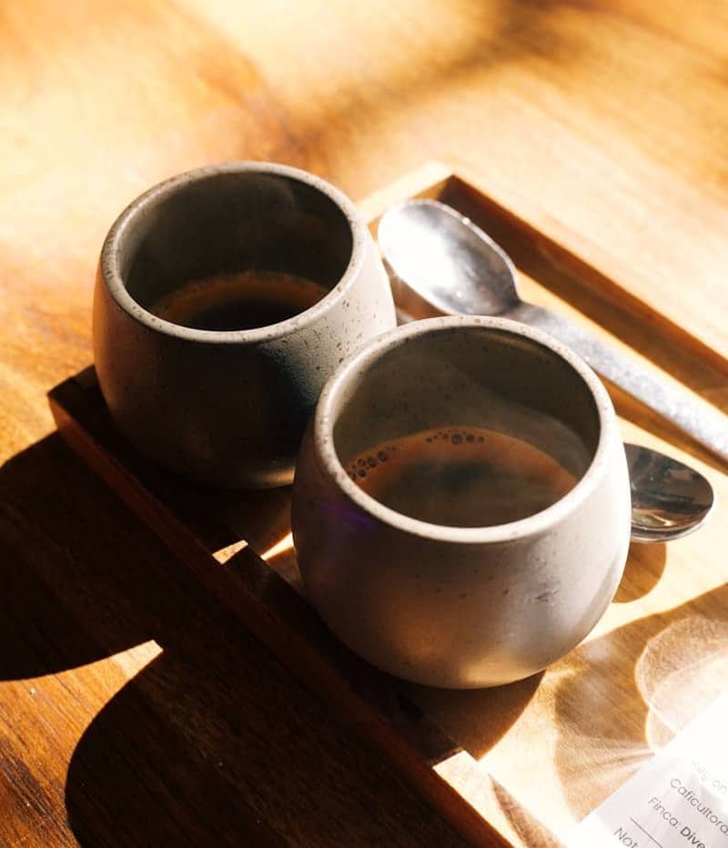Two cups of coffee sit on a wooden tray.
