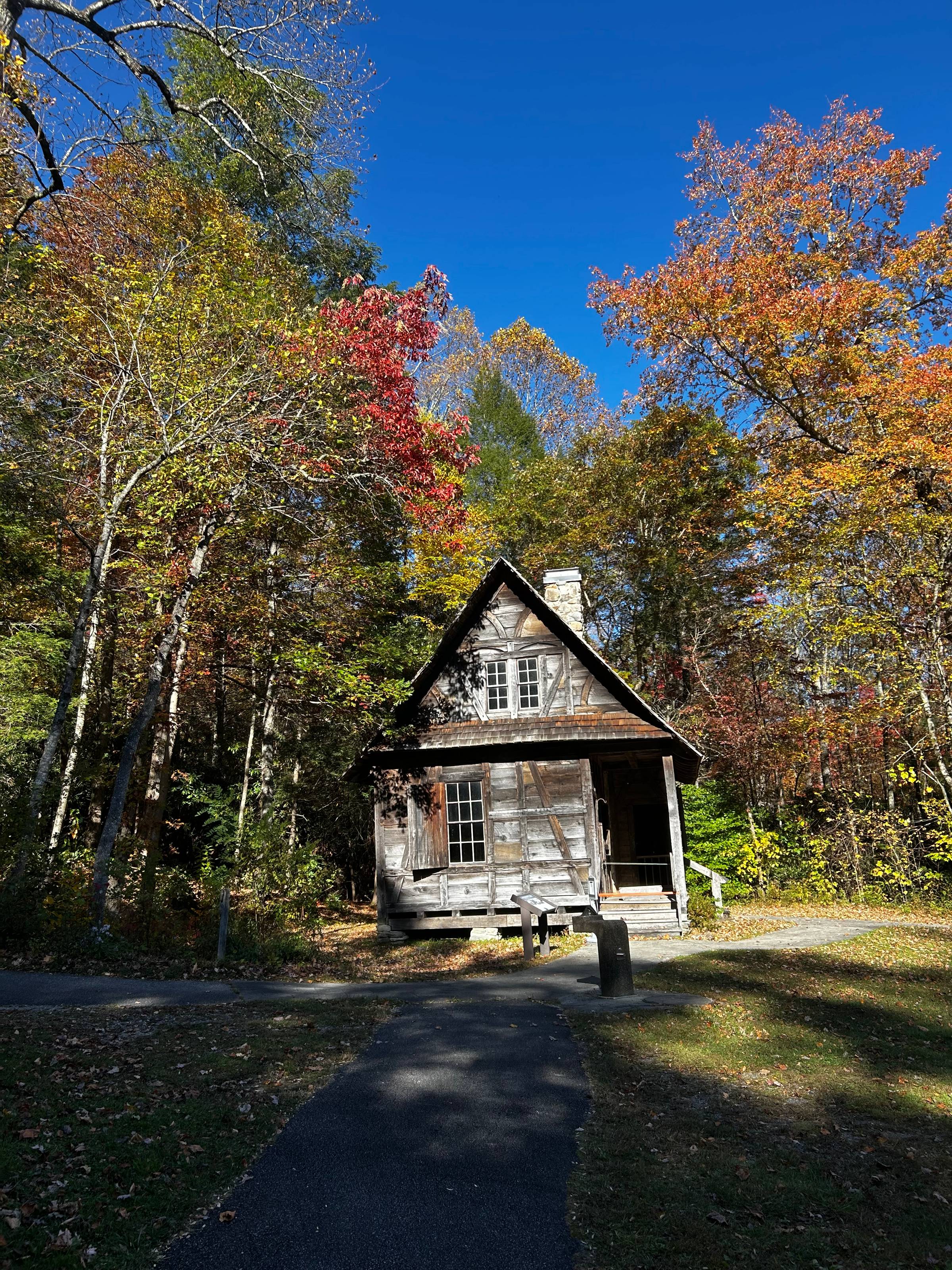 A photo of a rustic cabin in NC with a bright blue sky and colorful leaves on the trees around the cabin.