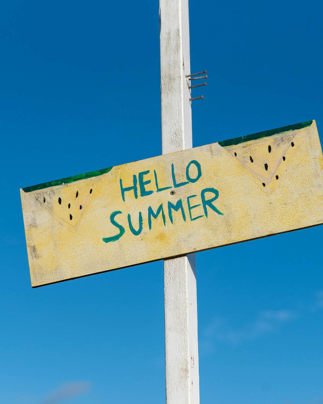 A wooden sign with "Hello Summer" painted on it.