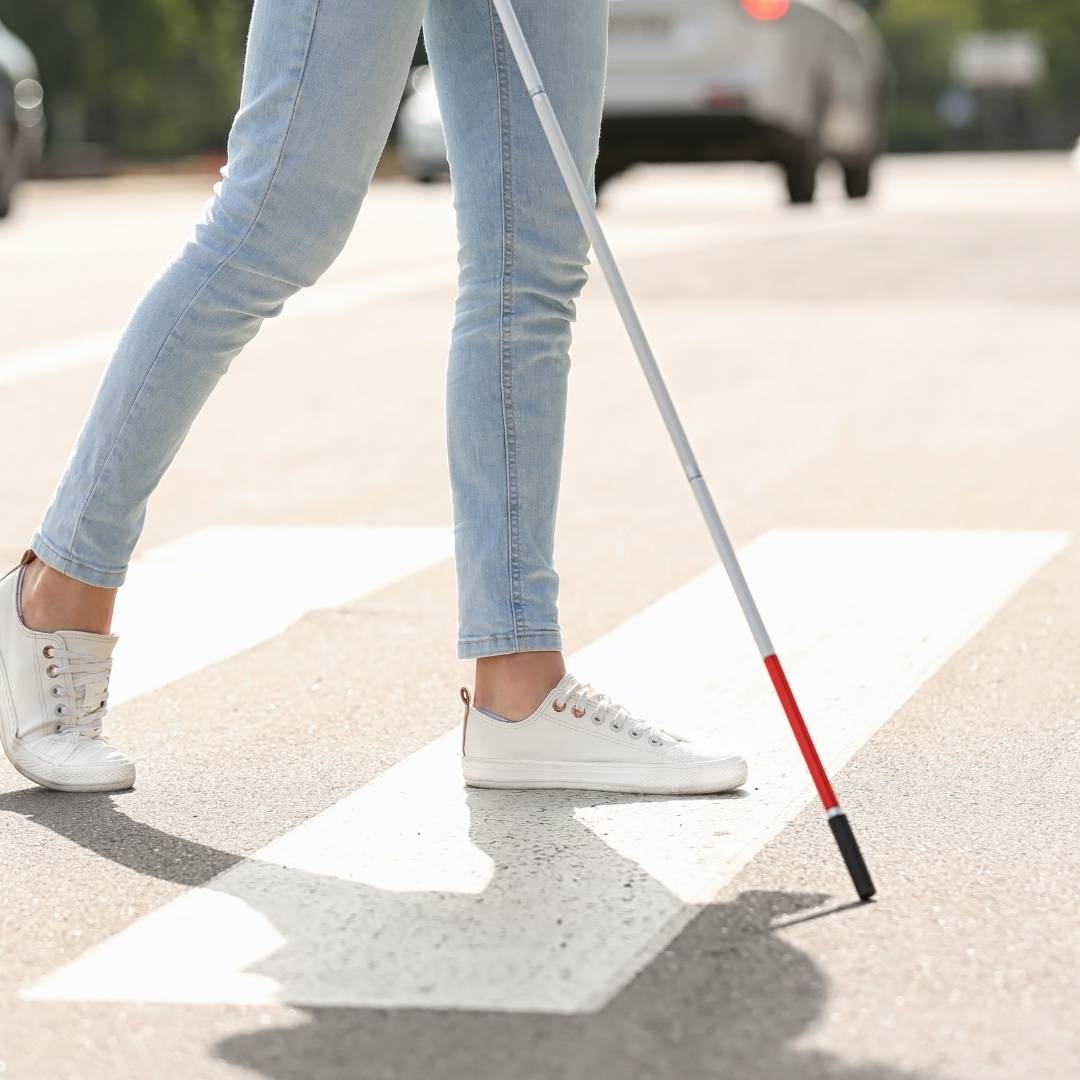 a photo of the feet of someone walking across the street using a white cane