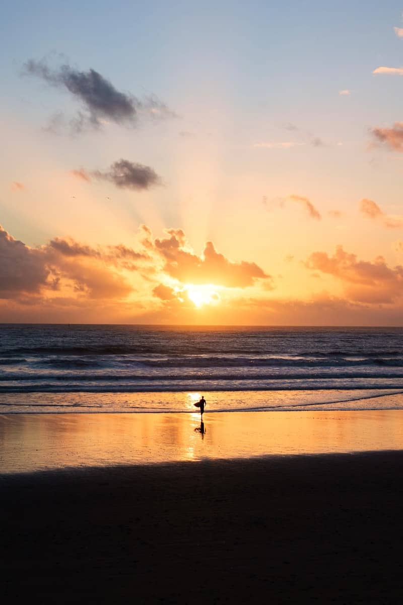 Surfer walking on beach at sunset