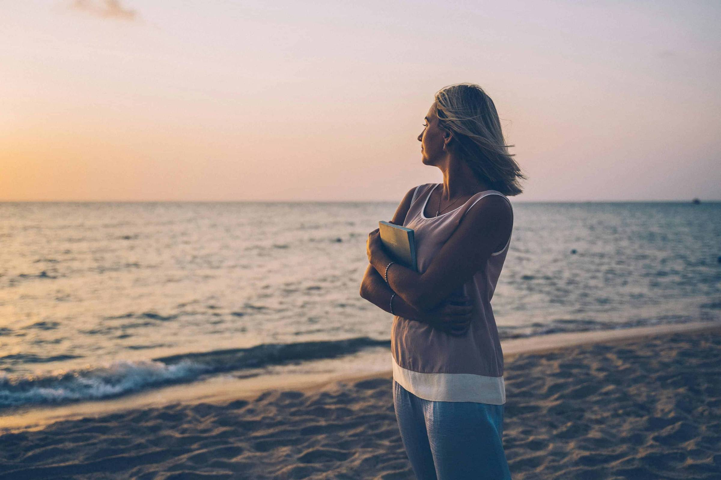 Wona holding journal staring at ocean at dusk