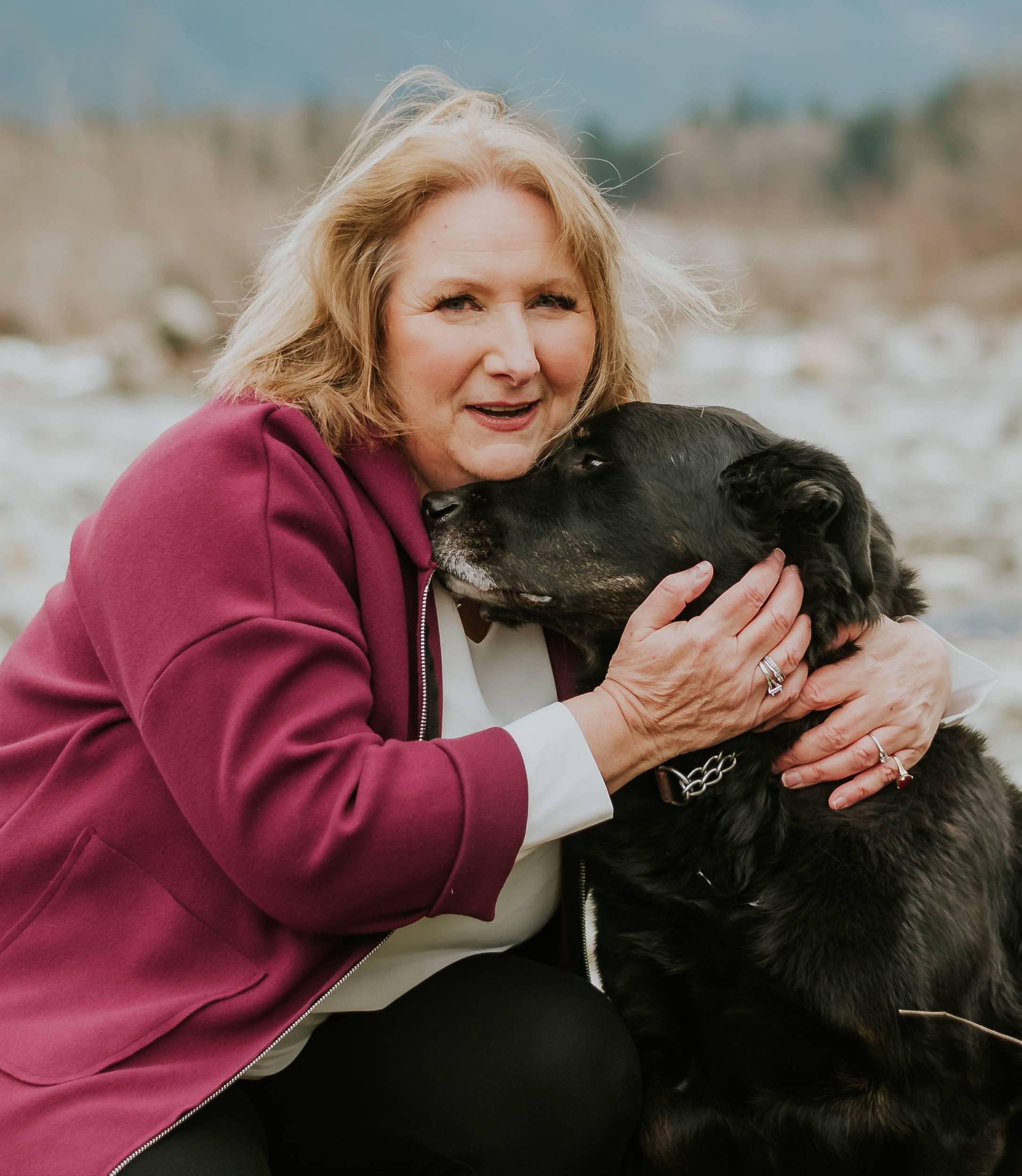 woman with her dogs face nestled into her neck out in nature