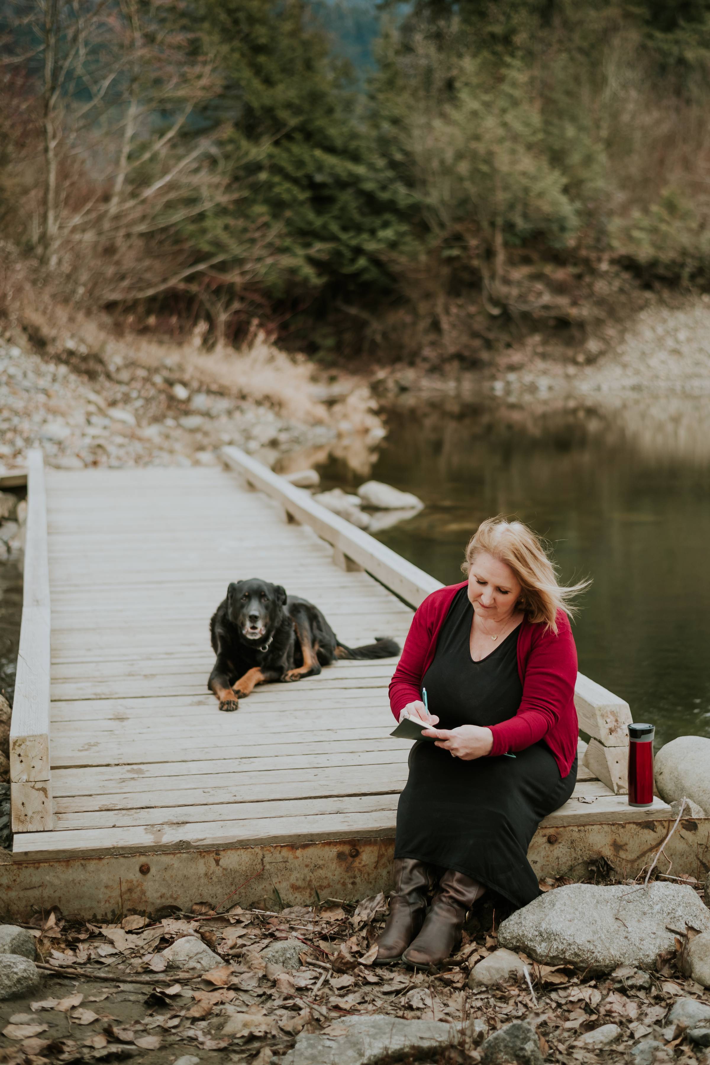 woman sitting on wooden bridge journalling with her dog