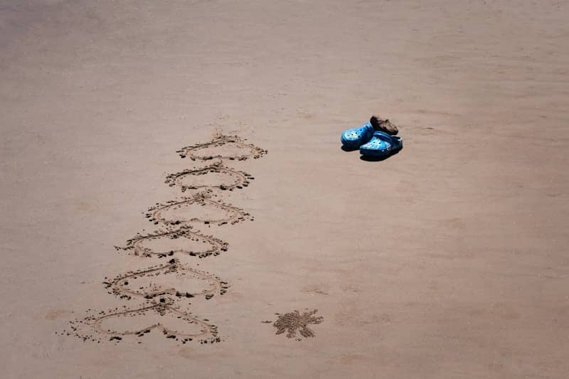 Hearts drawn in sand with a pair of blue flip-flops.