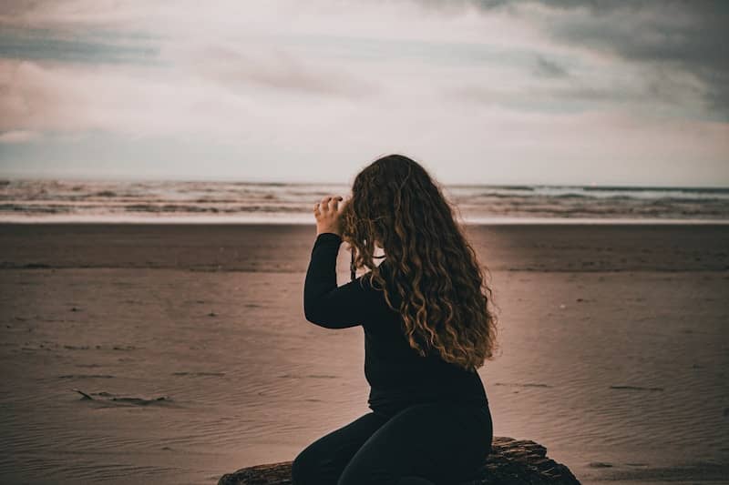 A woman sitting on top of a rock near the ocean