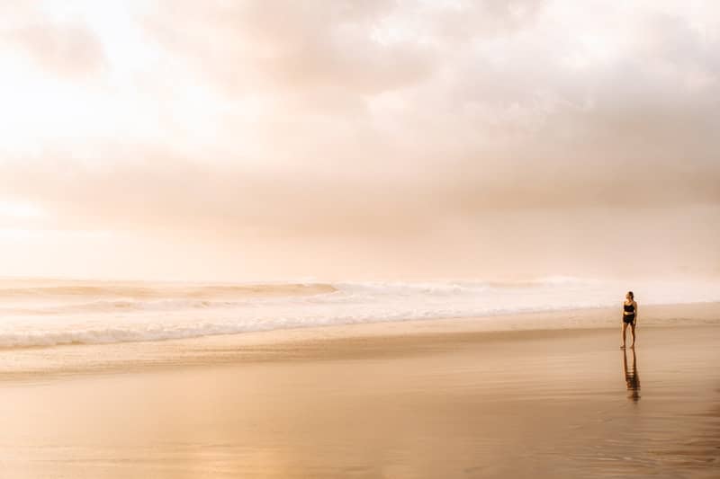 A person walks on a sandy beach at sunset.