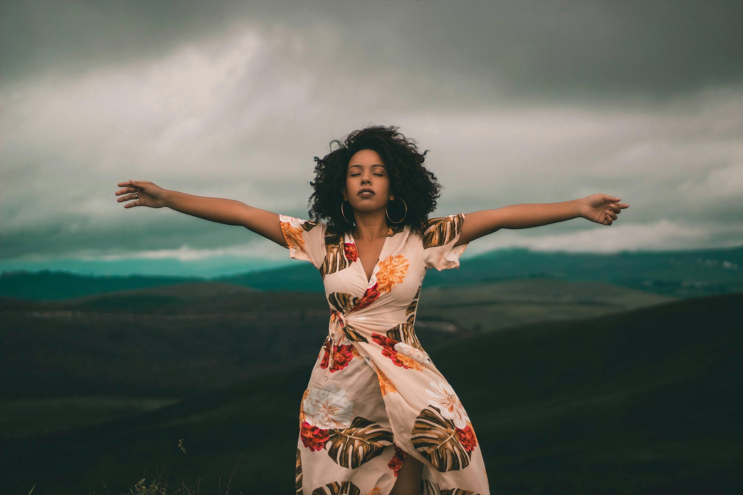 black woman with curly hair, eyes closed and arms open in the wind