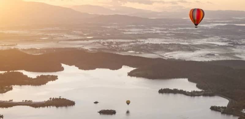 Hot air balloons fly over a serene lake at sunrise.