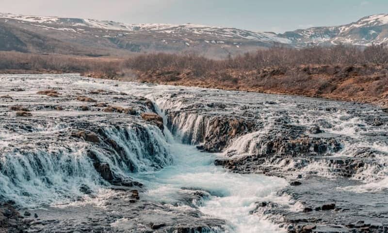 Waterfalls cascade into a river, surrounded by mountains.
