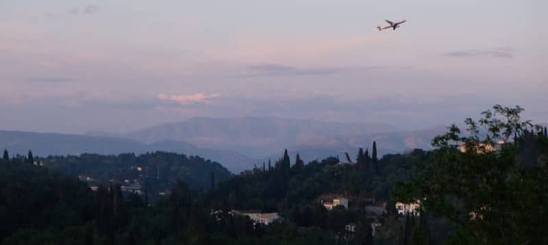 An airplane flies over a hilly, dusky landscape.