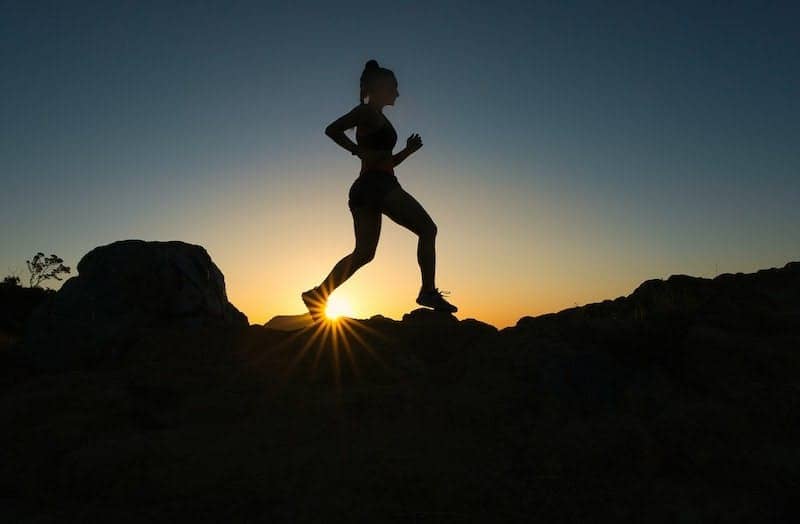 silhouette of man jumping on rocky mountain during sunset