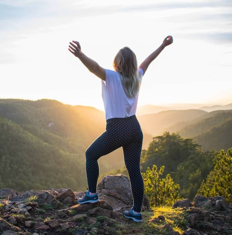 woman in white shirt and black pants standing on rocky mountain during daytime