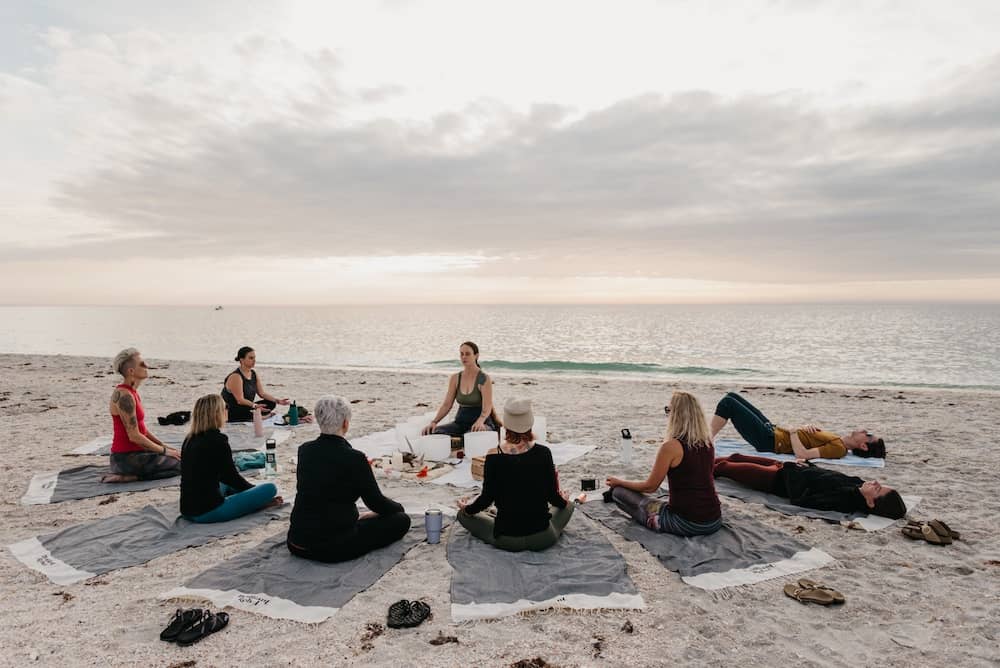 Brilliant Rebels sitting on blankets in a sound bath and meditation on the ocean at sunset