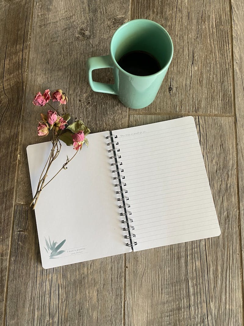 white notebook beside white ceramic mug on brown wooden table