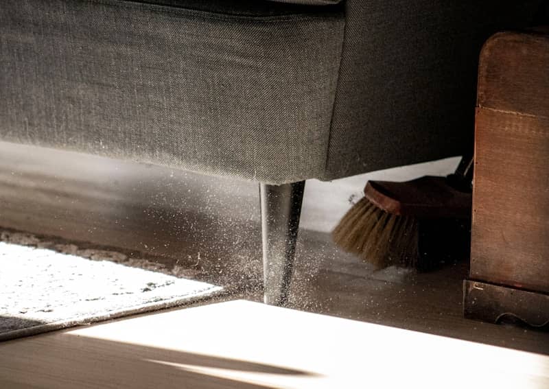 The image shows the base of a gray sofa with slim black legs, lit by sunlight that highlights floating dust particles