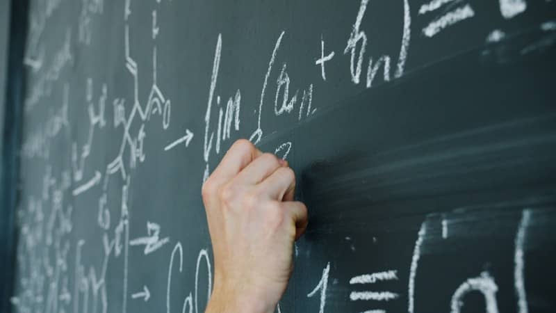 Hand writing mathematical formulas on a blackboard with chalk.