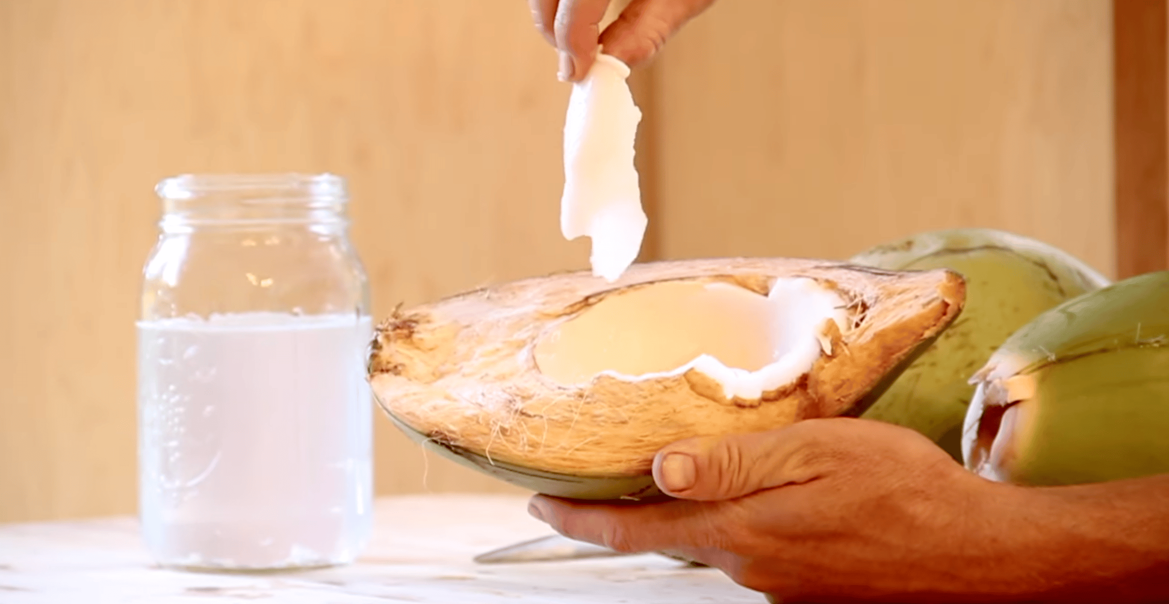 A person pulling out a thin gelatinous layer of coconut meat out of a green young coconut 